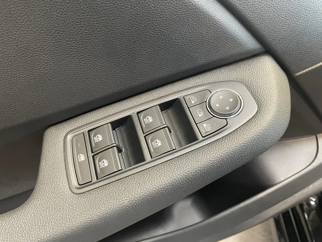 Gros plan sur la commande des vitres électriques et rétroviseurs sur la porte côté conducteur d’une Renault Clio noire étoile.