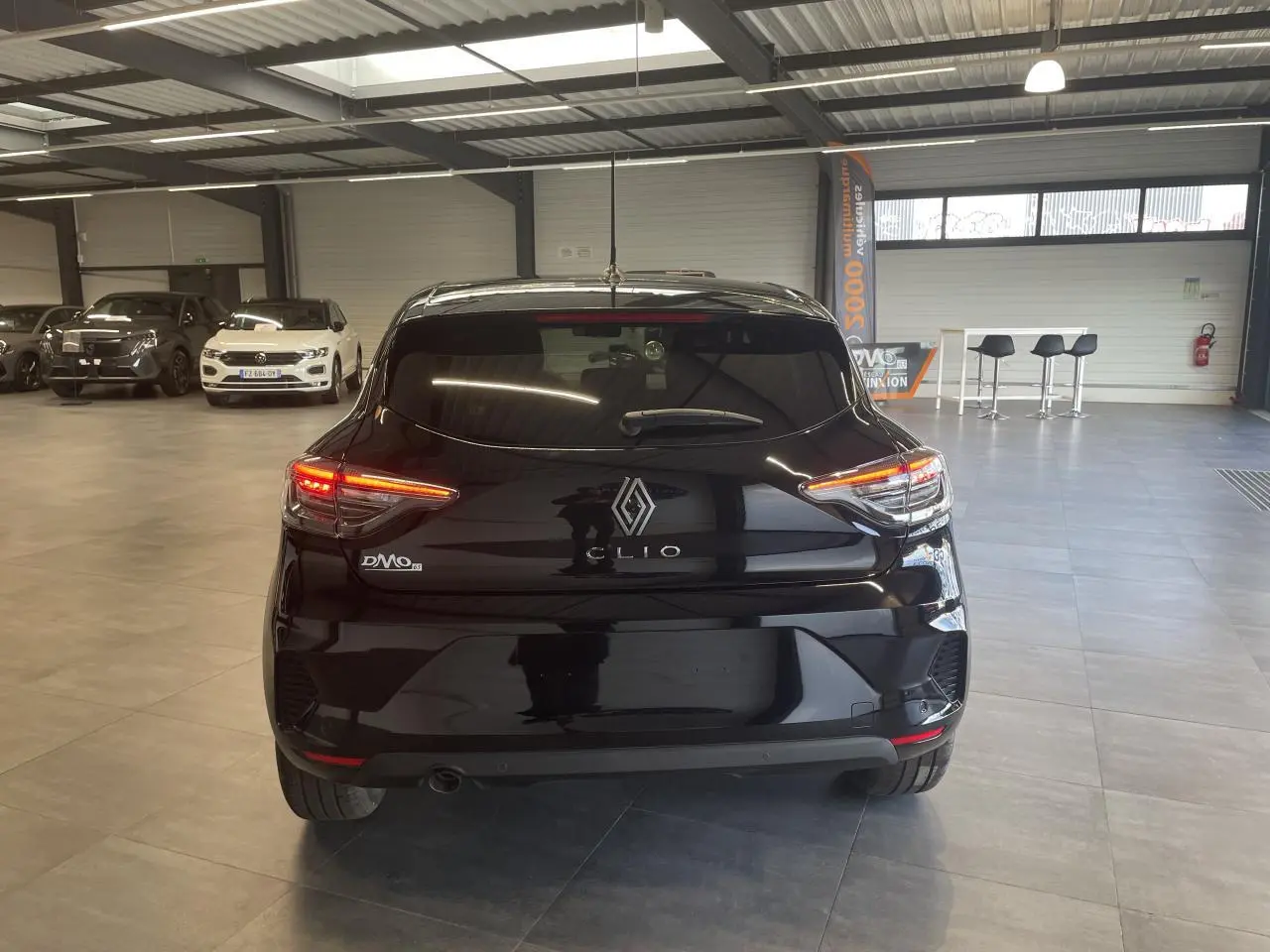 Vue arrière d'une Renault Clio 1.5 Blue dCi noire étoile avec feux LED allumés en intérieur showroom.