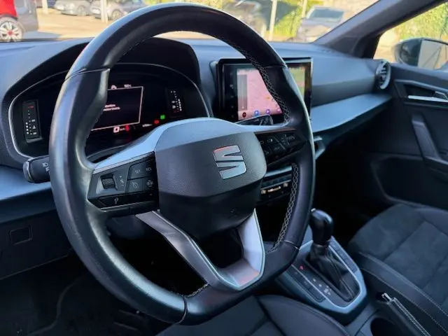 Vue intérieure centrée sur le volant cuir noir du SEAT Arona 2022 avec tableau de bord digital et écran tactile central.