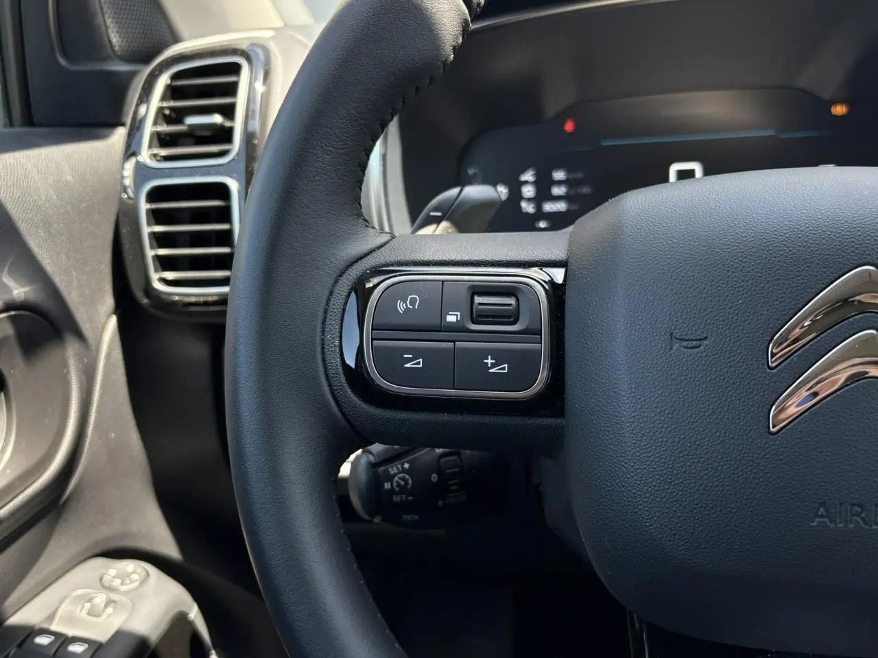 Gros plan sur le volant noir de la Citroën C5 Aircross Hybrid 2025, avec commandes intégrées côté gauche et aérateurs chromés.
