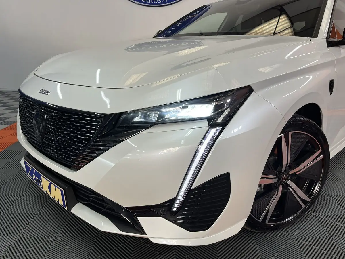 Vue 3/4 avant droit d'une Peugeot 308 GT PHEV blanche nacrée avec phares LED et jantes alliage noires.
