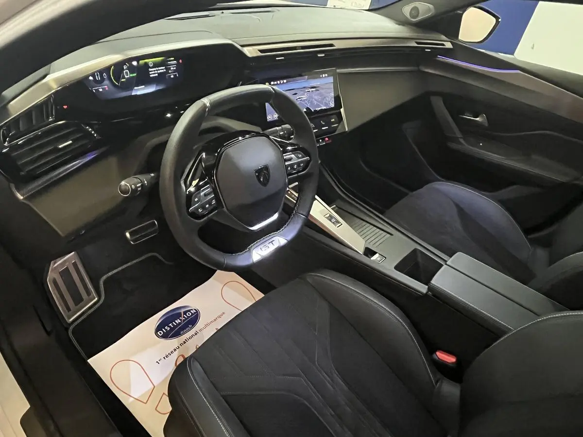 Intérieur noir de la Peugeot 308 GT PHEV 2022 vu côté conducteur, tableau de bord numérique et écran tactile central visibles.