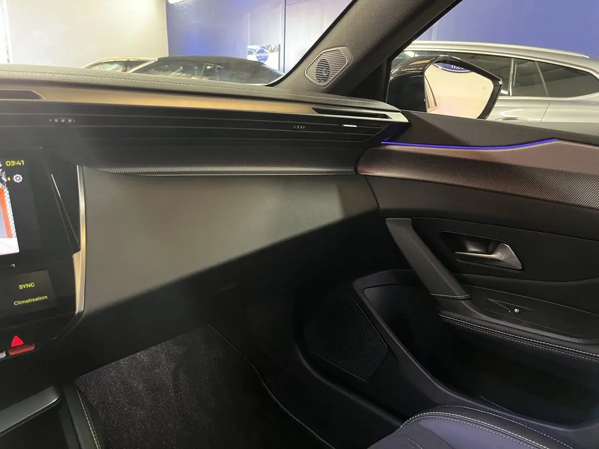 Intérieur côté passager de la Peugeot 308 GT PHEV 180 blanc nacré avec éclairage d'ambiance bleu et tableau de bord moderne.