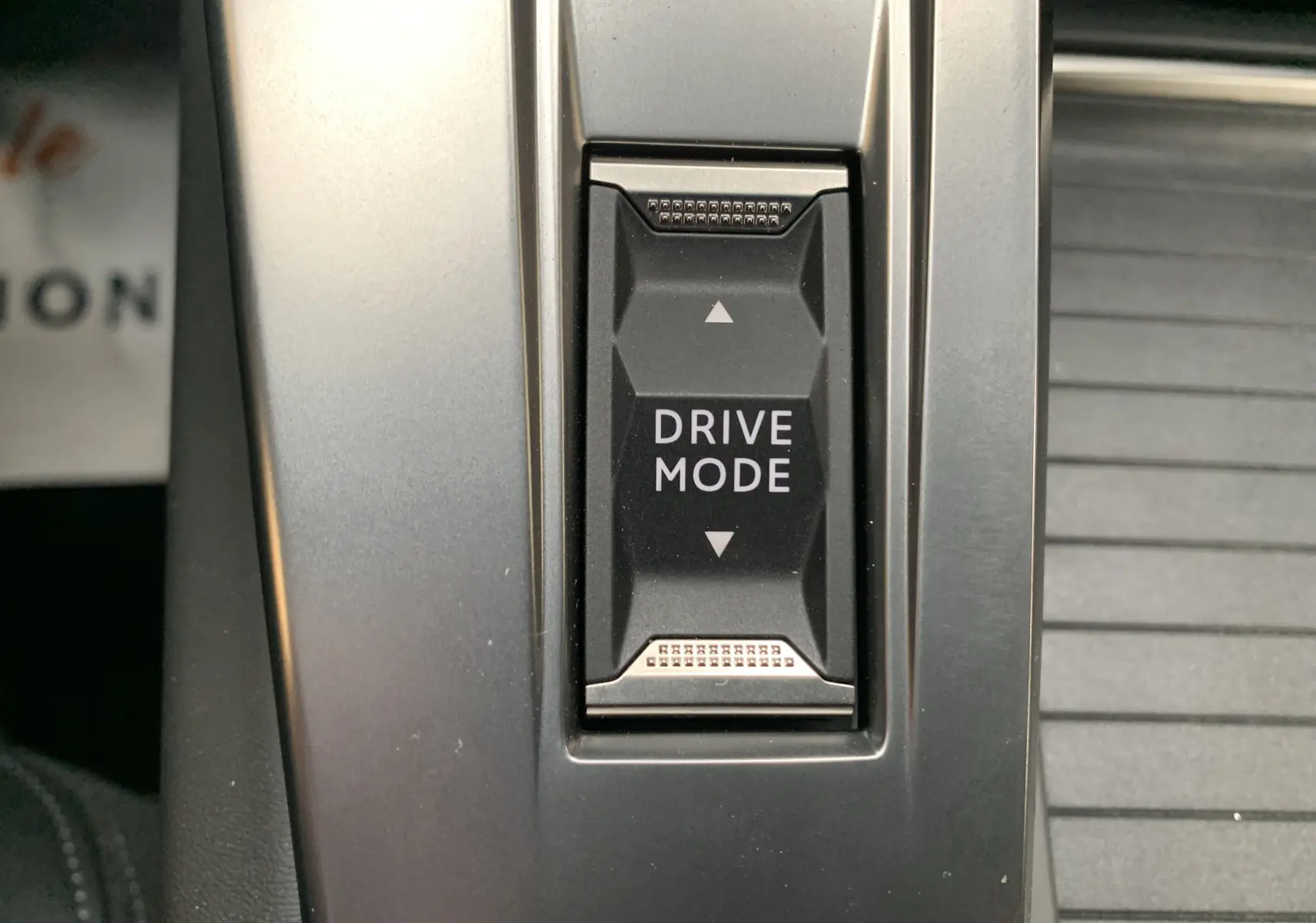 Gros plan sur le bouton Drive Mode au centre de la console d'une Peugeot 308 GT PHEV blanc nacré.