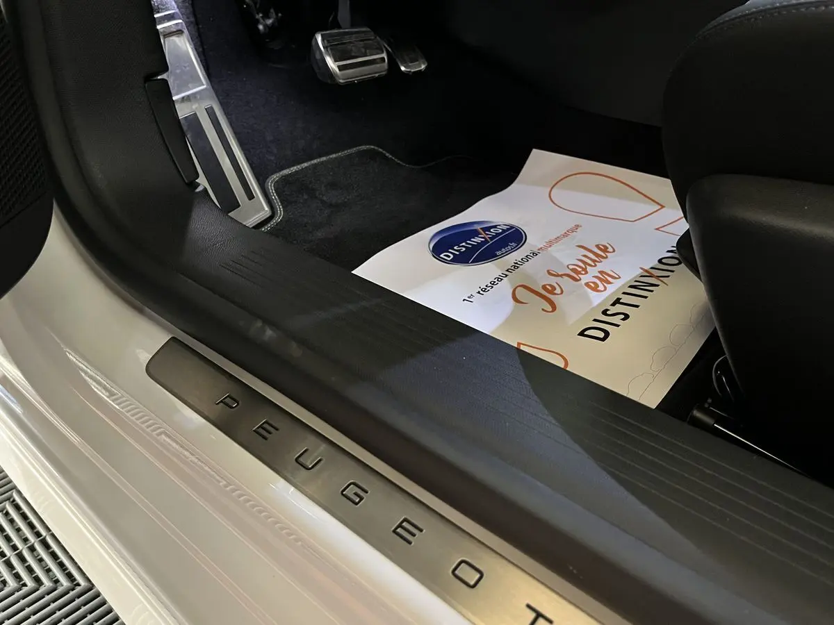 Détail intérieur côté conducteur avec seuil de porte Peugeot en métal sur carrosserie blanc nacré.