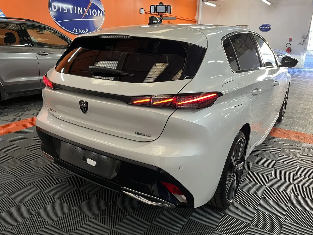 Vue 3/4 arrière droite d'une Peugeot 308 GT PHEV blanche nacrée avec feux LED allumés dans un showroom.