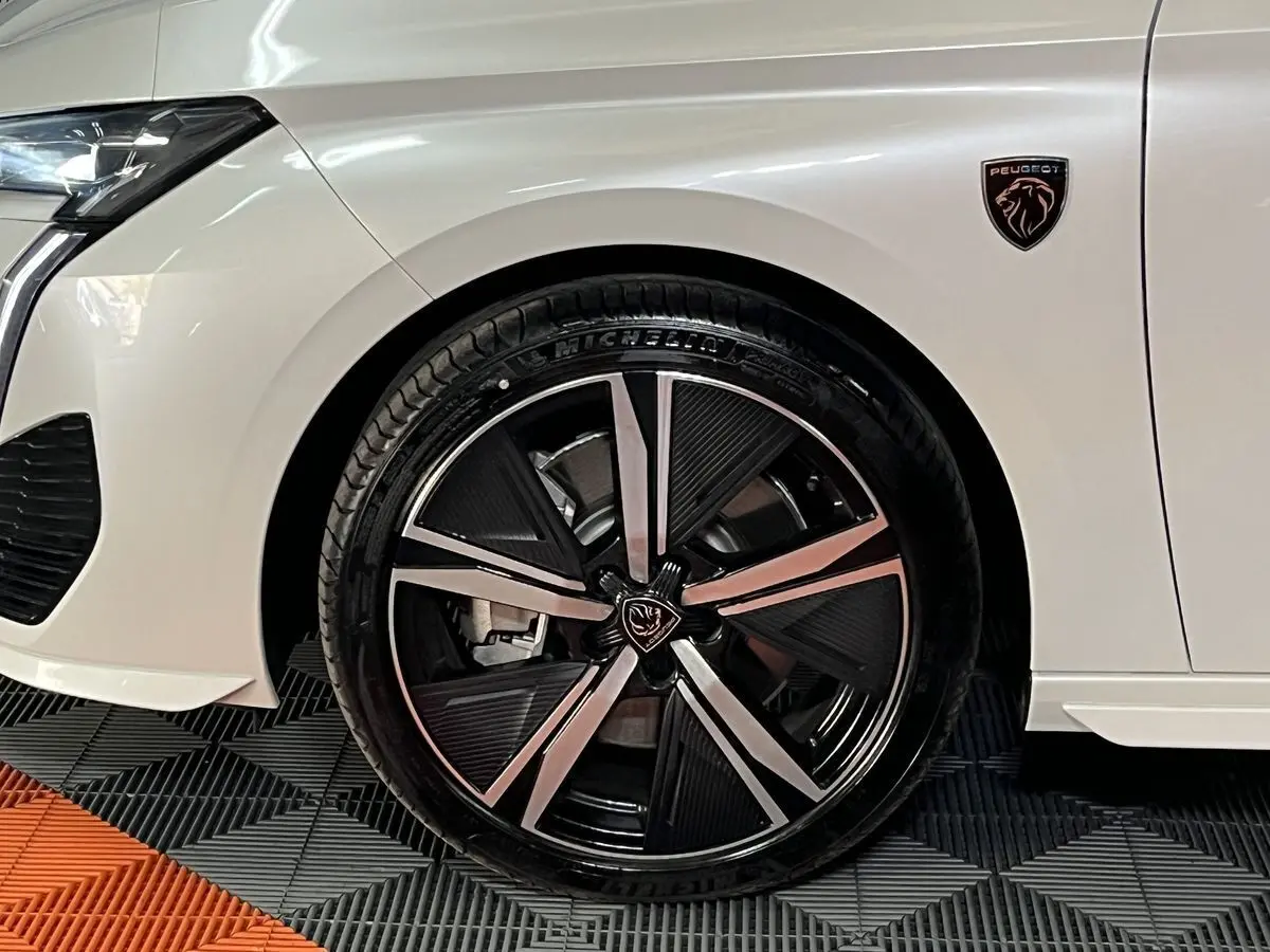 Gros plan sur la roue avant gauche et l’aile blanche nacrée d’une Peugeot 308 GT PHEV 2022 avec logo lion noir.