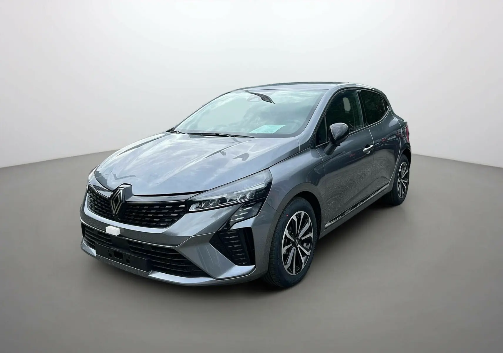 Renault Clio V TCE 90 TECHNO 2025 gris schiste vue 3/4 avant avec calandre noire et jantes alliage distinctives.