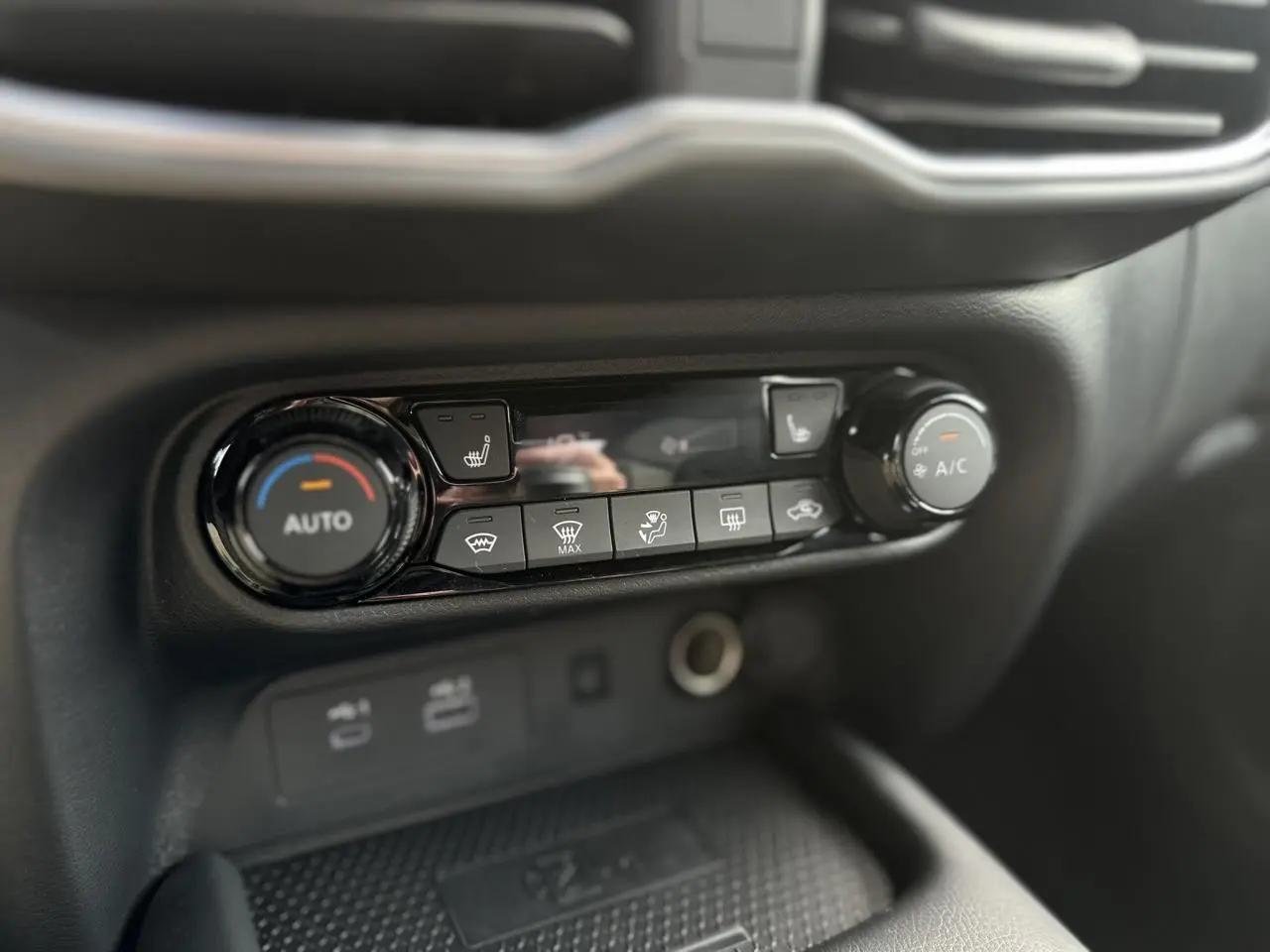 Gros plan sur la console centrale du Nissan Juke blanc nacré 2025, mettant en valeur les commandes de climatisation automatique et sièges chauffants.