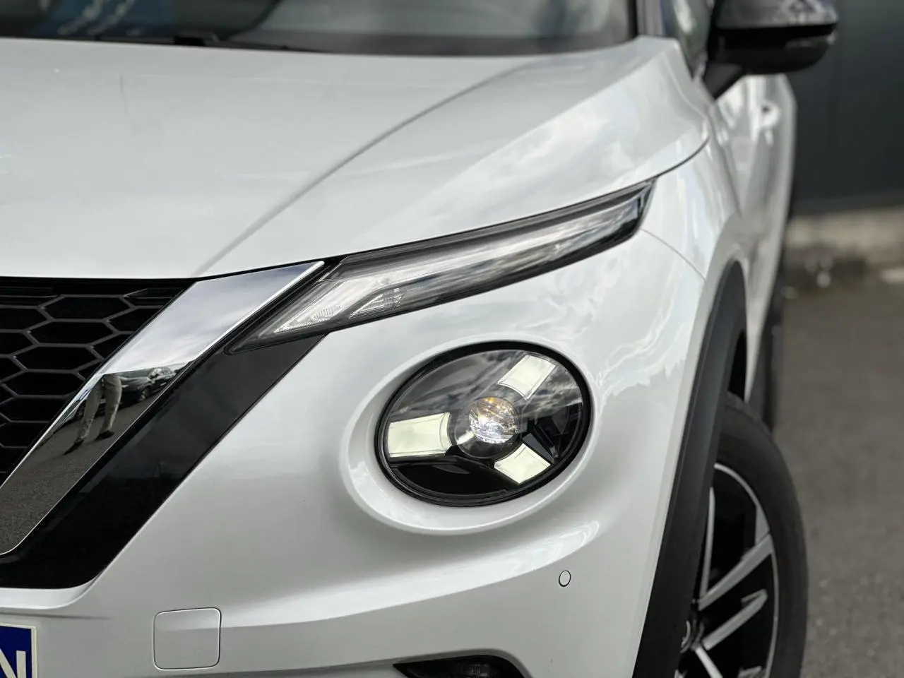 Gros plan sur l'avant droit blanc nacré du Nissan Juke 2025, mettant en valeur son phare rond et la calandre noire.