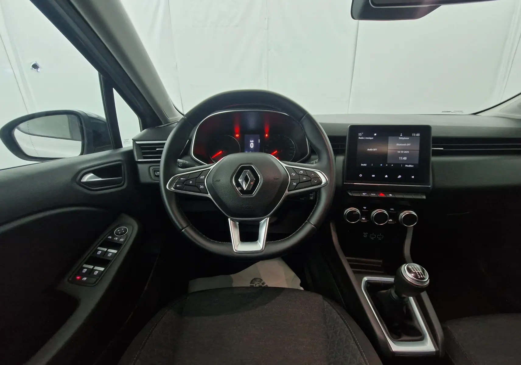 Intérieur de Renault Clio V gris platine, vue depuis le siège conducteur sur le volant, tableau de bord et levier de vitesse manuel.