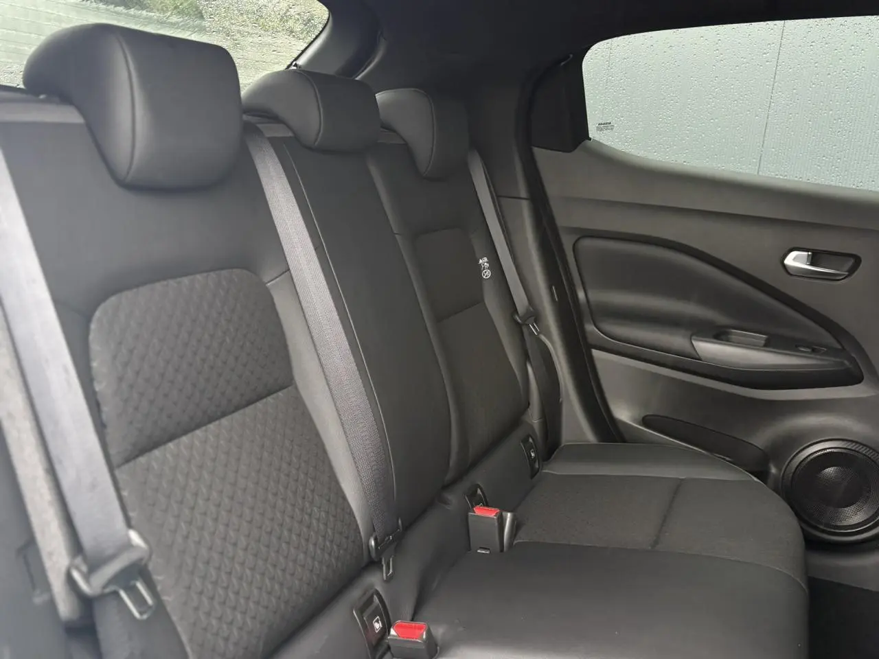 Vue latérale droite de la banquette arrière noire du Nissan Juke 2025 avec ceintures et haut-parleur intégré à la porte.