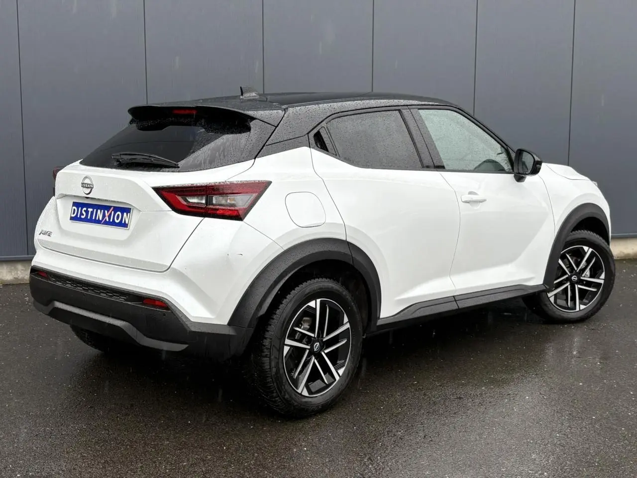 Nissan Juke blanc nacré en 3/4 arrière droit, toit noir contrasté et jantes alliage 17 pouces sous la pluie.