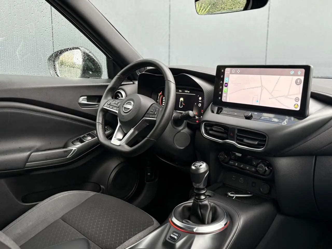 Vue intérieure côté conducteur du Nissan Juke blanc nacré 2025, avec tableau de bord digital et écran tactile GPS.