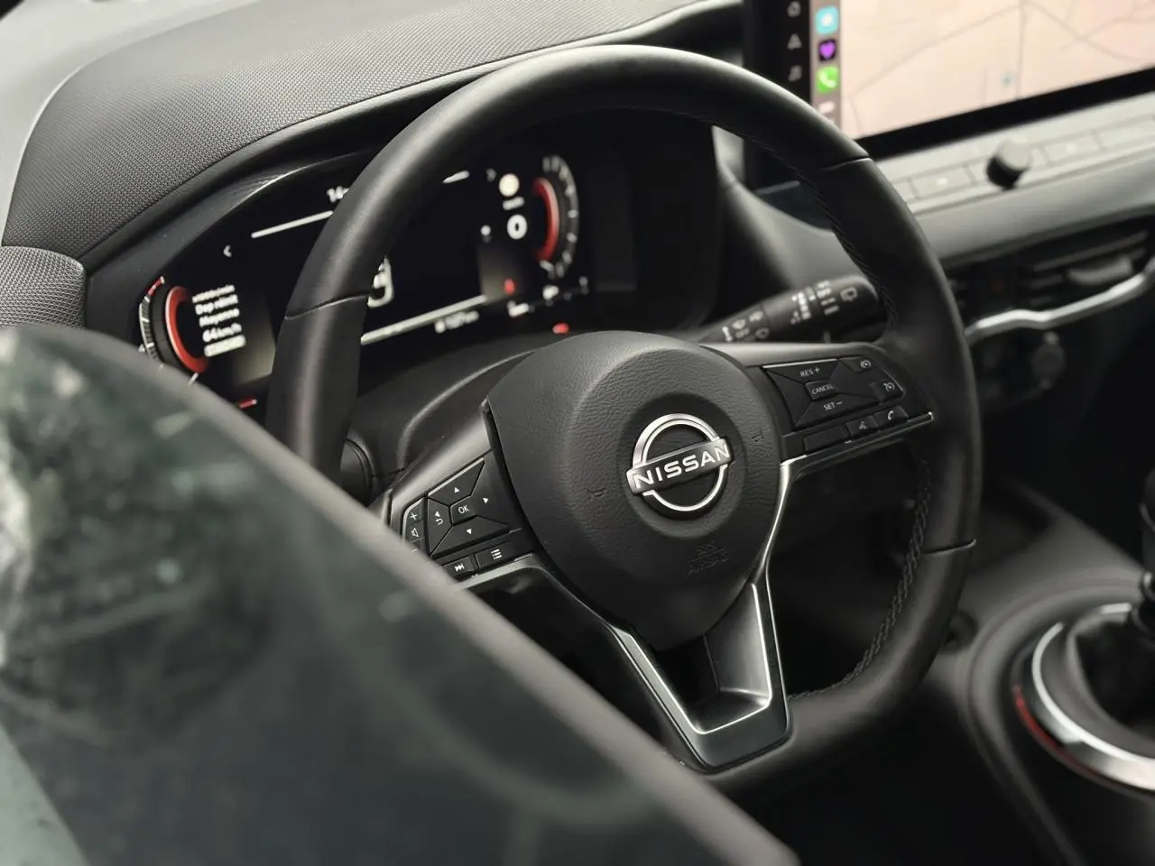 Vue rapprochée du volant en cuir noir et du tableau de bord digital du Nissan Juke blanc nacré 2025.