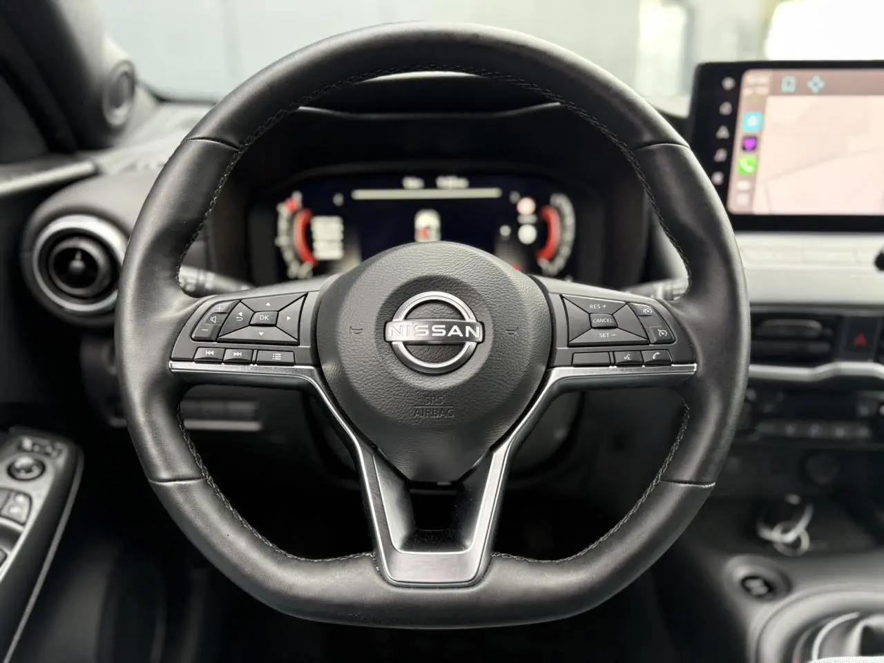 Volant en cuir noir de Nissan Juke 2025 avec commandes intégrées, tableau de bord digital et écran tactile visible en arrière-plan.