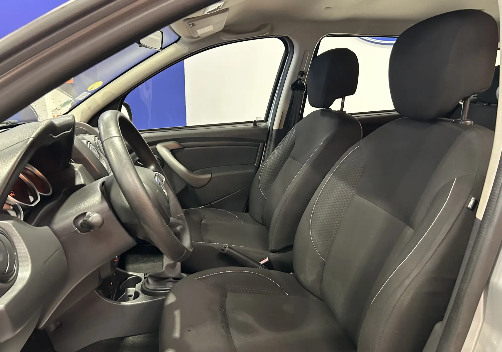 Vue intérieure côté conducteur du Dacia Duster 2017 gris, sièges tissu noirs et volant multifonction.