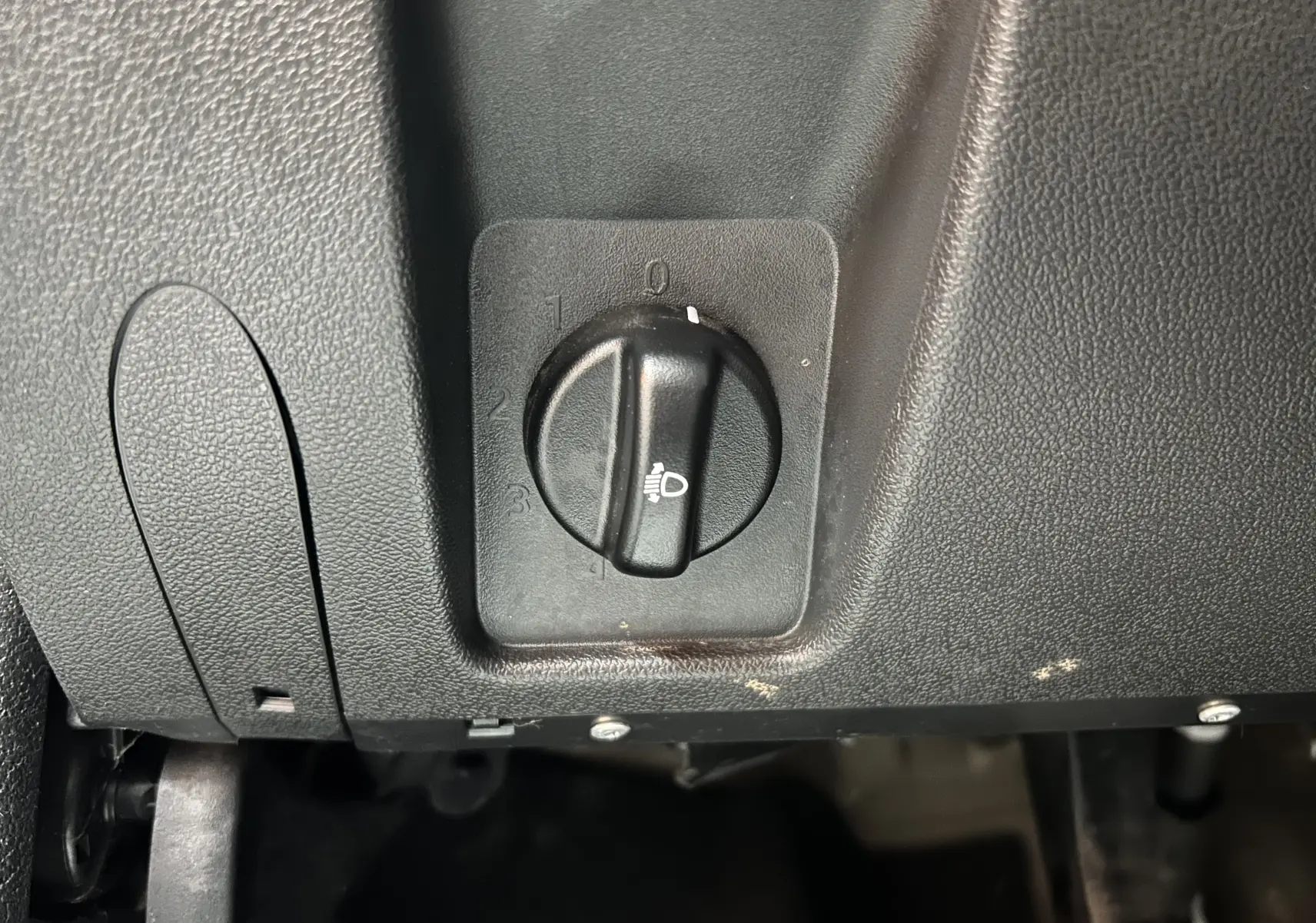 Gros plan sur le bouton de réglage de l'intensité des phares dans l'habitacle noir du Dacia Duster gris 2017.