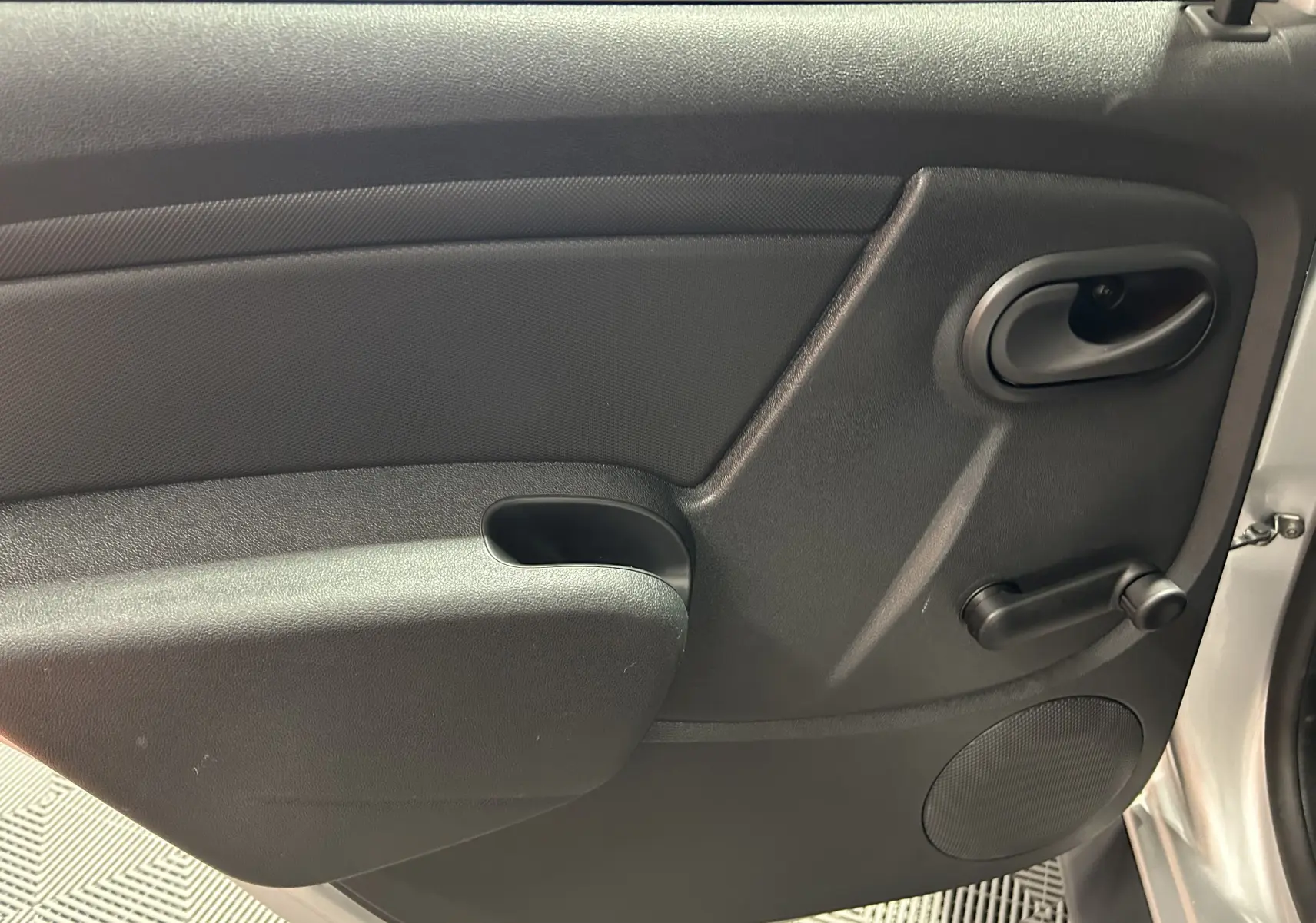 Gros plan sur la porte intérieure côté droit du Dacia Duster gris 2017, avec poignée et manivelle de vitre manuelle.