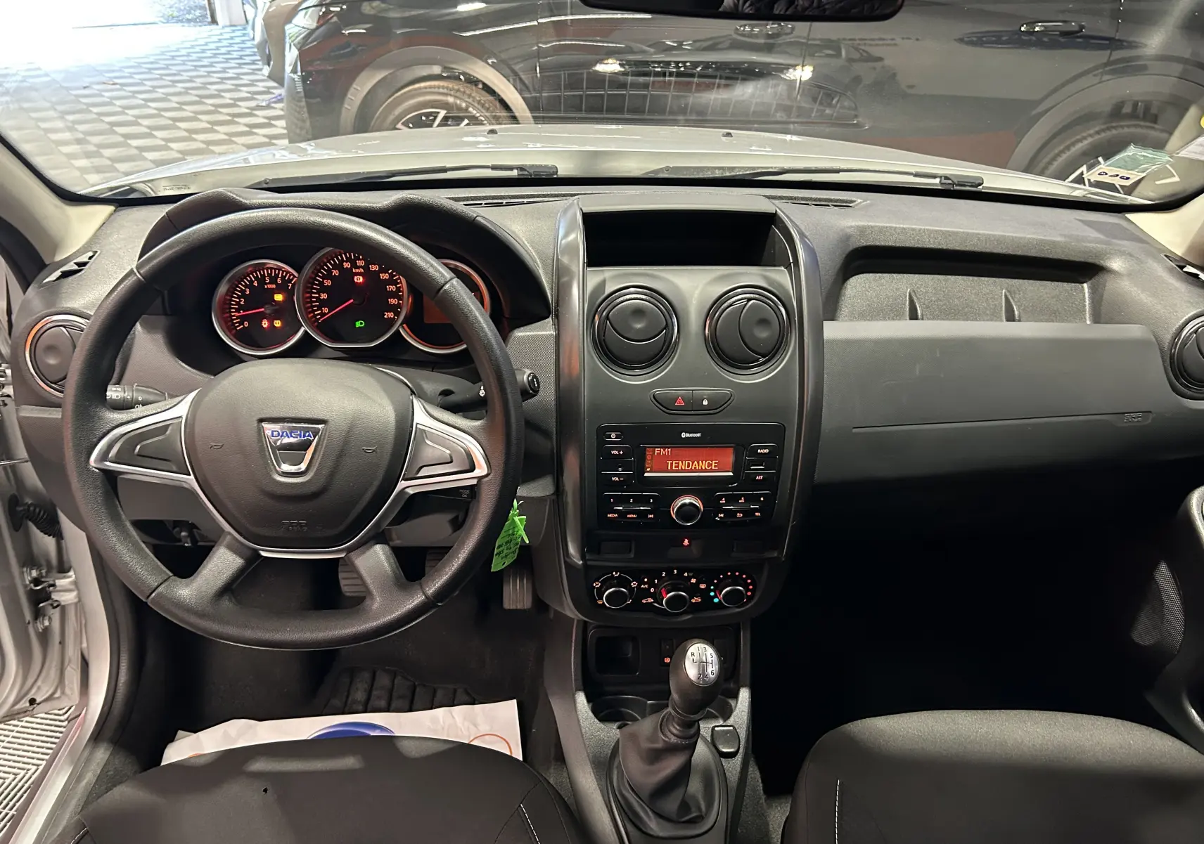 Vue intérieure du tableau de bord et volant noir du Dacia Duster gris 2017 avec console centrale et levier de vitesses manuel.