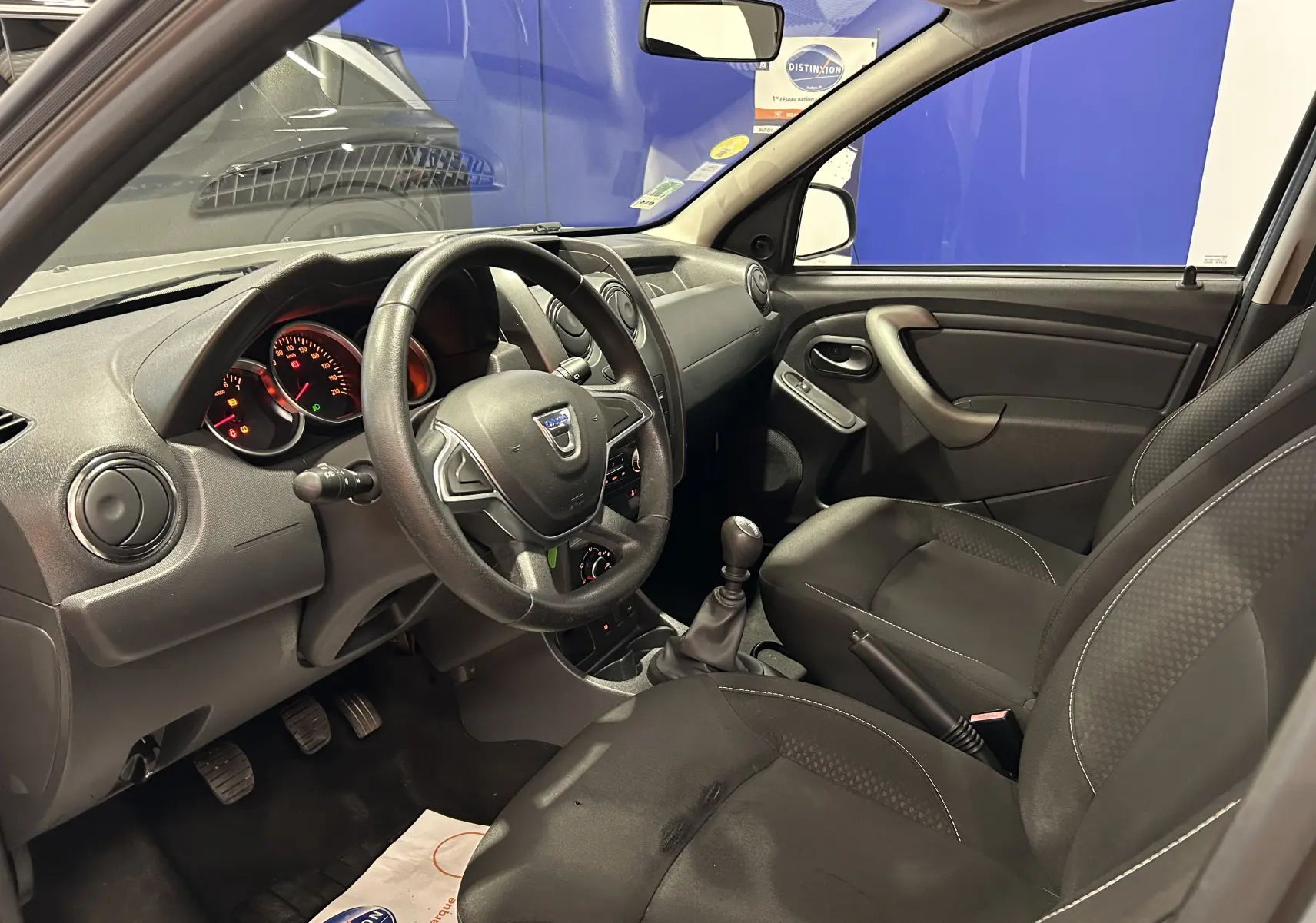 Intérieur avant droit du Dacia Duster gris 2017, volant cuir, tableau de bord simple et sièges tissu noirs.