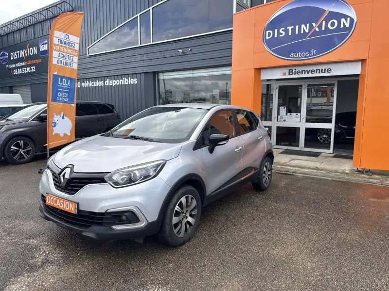 Renault Captur gris platine en 3/4 avant droit devant un concessionnaire Distinxion avec plaque occasion visible.