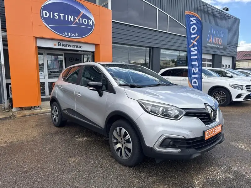 Renault Captur gris platine en 3/4 avant droit, stationné devant un concessionnaire avec panneau orange "Distinxion".