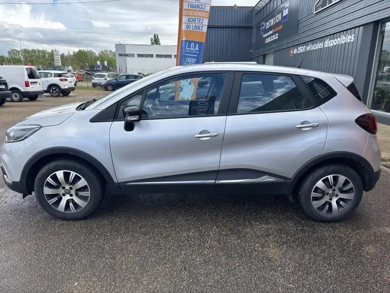 Profil côté droit d'un Renault Captur gris platine de 2019 avec jantes alliage et protections noires basses.