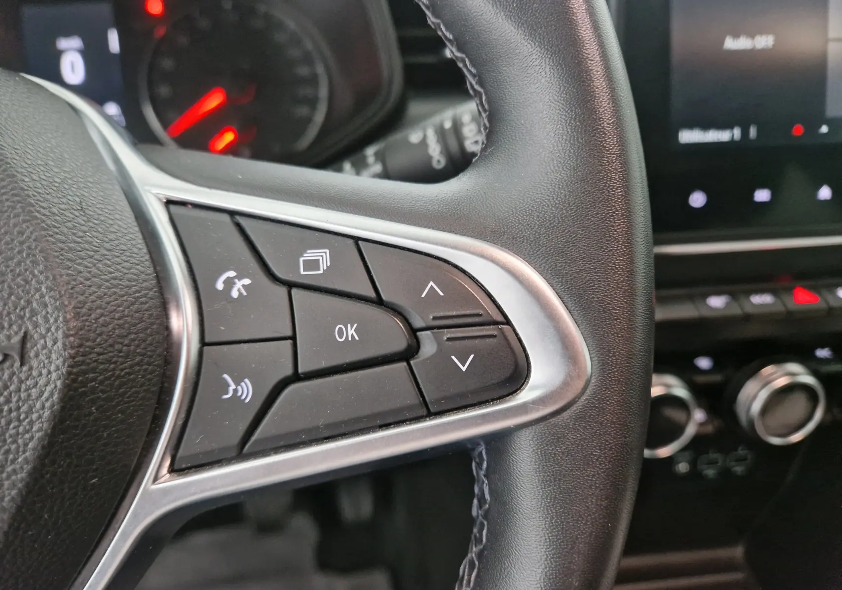 Gros plan sur les commandes du volant côté gauche d'une Renault Clio V gris platine, tableau de bord en arrière-plan.