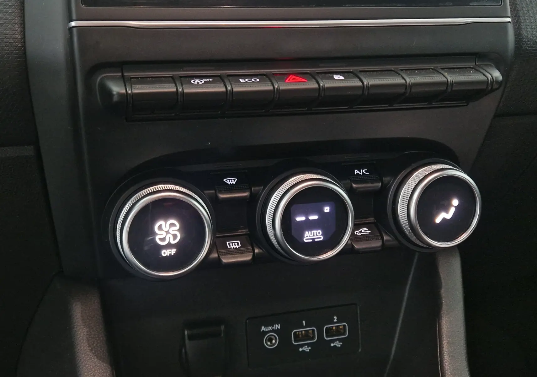 Gros plan sur les commandes de climatisation et les boutons de fonction du tableau de bord d’une Renault Clio V gris platine.