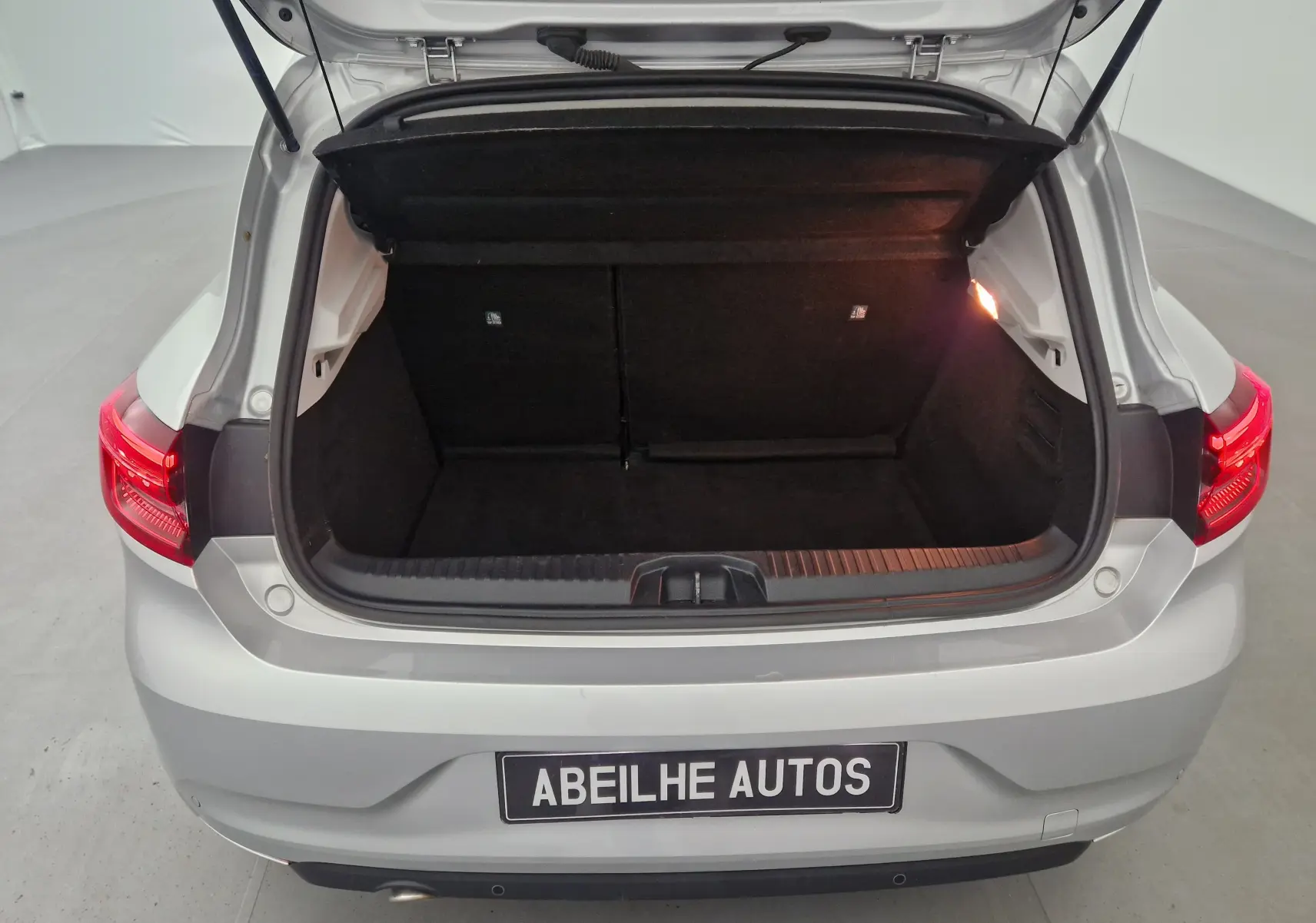 Coffre ouvert vu de l'arrière d'une Renault Clio V gris platine avec feux arrière allumés et intérieur de coffre noir.