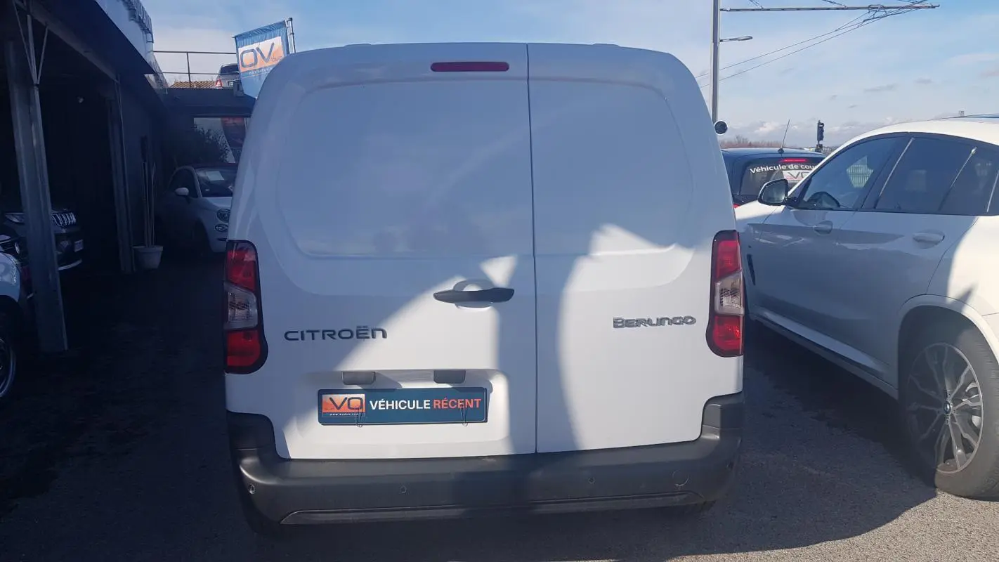 Vue arrière d’un utilitaire Citroën Berlingo blanc avec portes battantes et pare-chocs noir, stationné en extérieur.