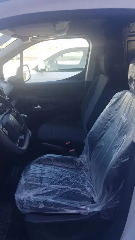 Vue intérieure côté conducteur du Citroën Berlingo blanc 2025, siège protégé par housse plastique, volant multifonctions visible.