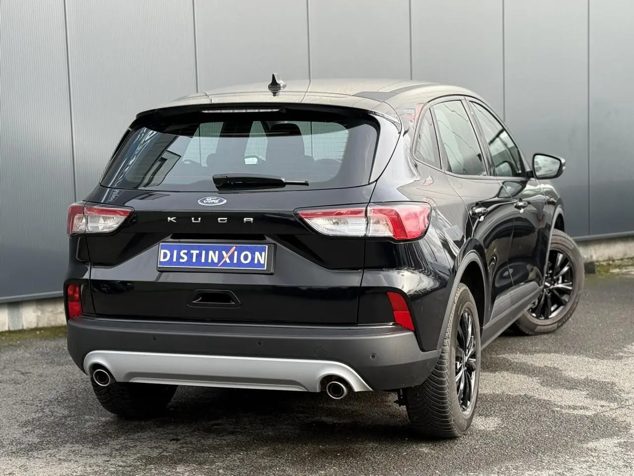 Vue 3/4 arrière droite d'un Ford Kuga noir Obsidien avec jantes alliage noires et double sortie d'échappement.