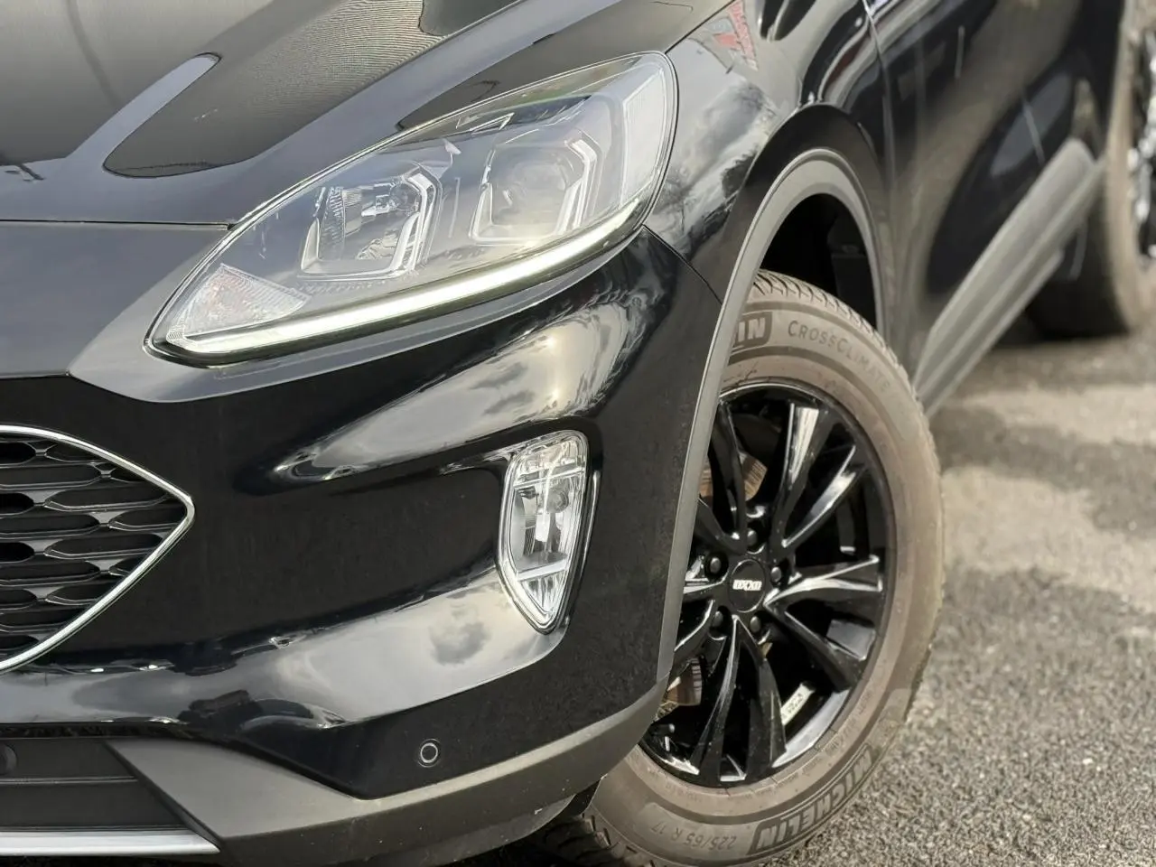 Gros plan sur l’avant droit du Ford Kuga noir Obsidien 2024, mettant en valeur le projecteur LED et la jante alliage noire.