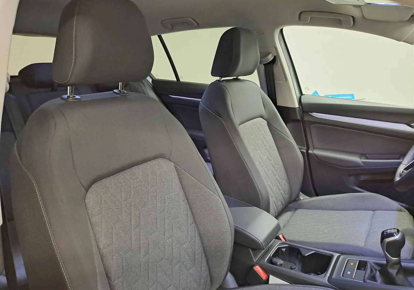 Vue intérieure rapprochée des sièges avant en tissu gris de la Volkswagen Golf 1.5 eTSI 2025, avec levier de vitesses manuel visible.