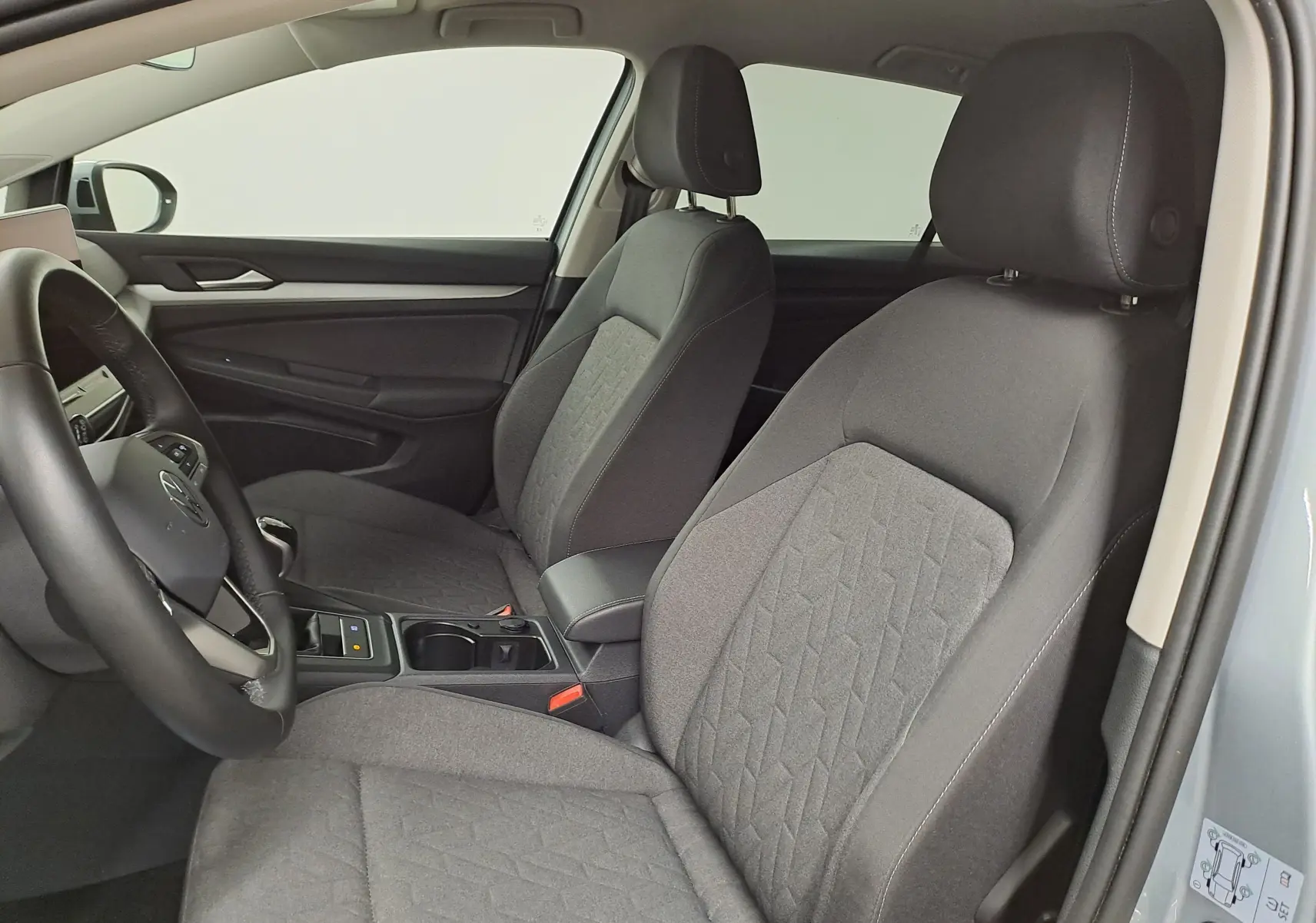 Vue intérieure côté conducteur de la Volkswagen Golf 1.5 eTSI 2025 avec sièges tissu gris et volant noir, portière argent Dolomite visible.