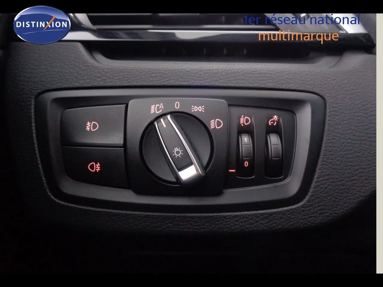 Gros plan sur le panneau de commande des phares du BMW X1 blanc Alpine Metal, avec réglages éclairage et antibrouillard.