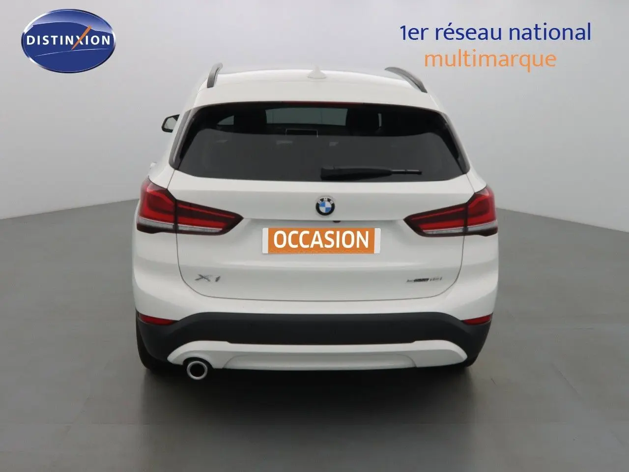 Vue arrière d'un BMW X1 blanc Alpine Metal avec feux rouges et sortie d'échappement unique côté gauche.