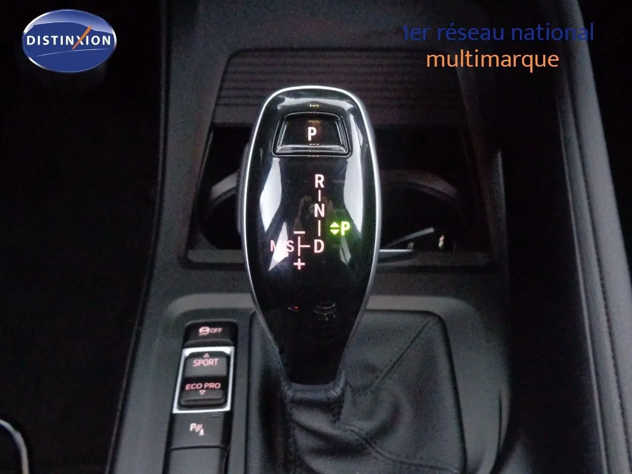 Le levier de vitesses automatique noir brillant de la BMW X1 blanc Alpine, vu en gros plan intérieur.