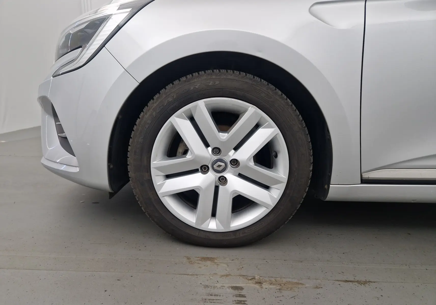 Gros plan sur la roue avant gauche d'une Renault Clio V gris platine, mettant en valeur la jante au design moderne.