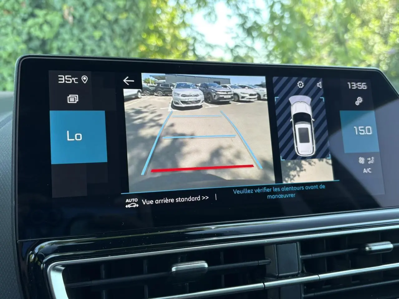 Écran tactile intérieur montrant la caméra de recul avec vue arrière d’un parking ensoleillé.