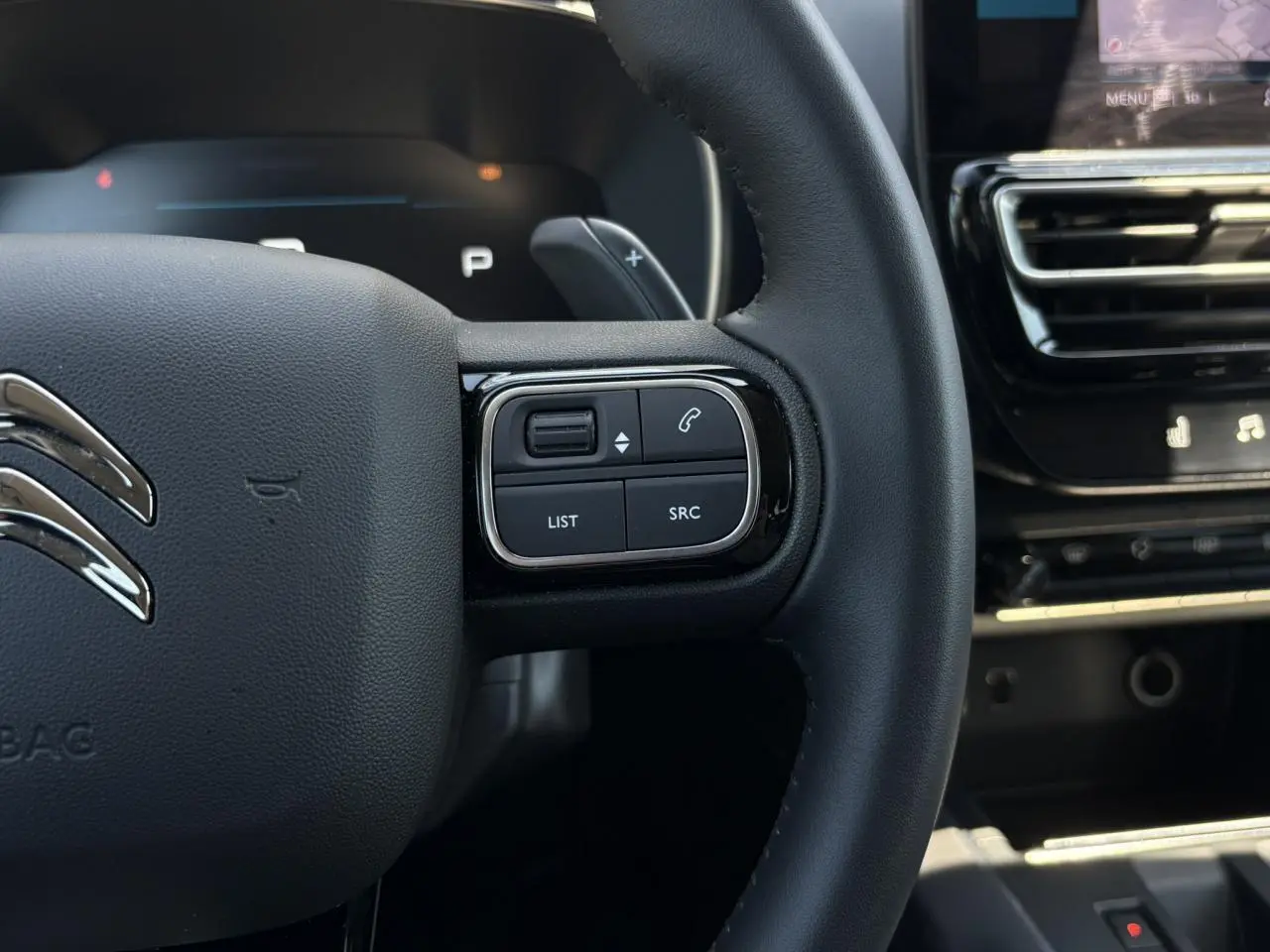 Gros plan sur le volant noir du Citroën C5 Aircross Hybrid 2025, avec commandes intégrées côté droit et tableau de bord partiel.