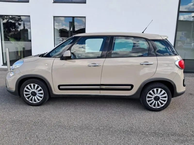 Profil côté gauche d'une FIAT 500L beige 2014 avec baguettes noires et jantes multirayons visibles.
