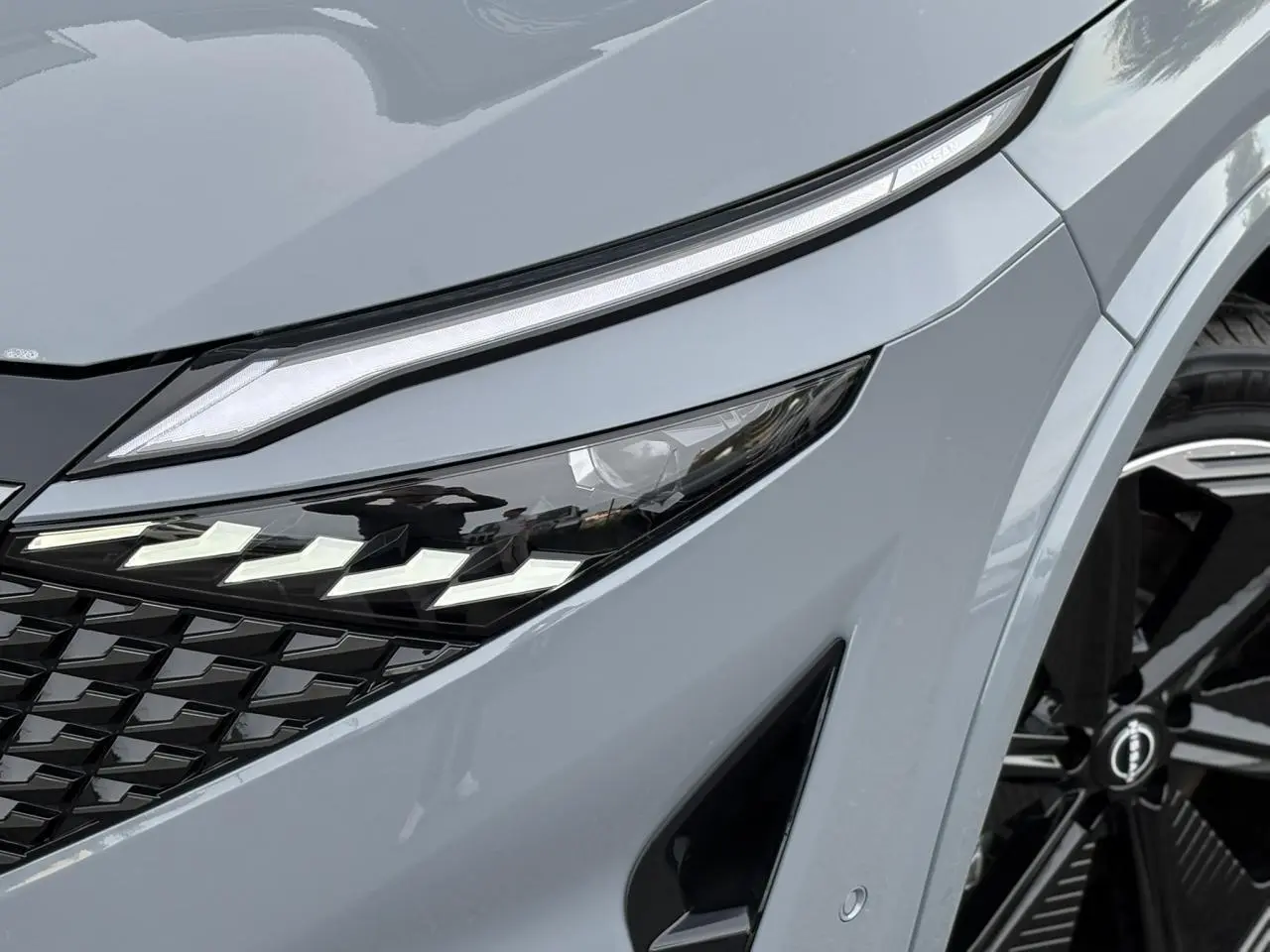 Gros plan sur le phare avant gauche du Nissan Qashqai gris Ceramic avec calandre noire et jante alliage 20 pouces.