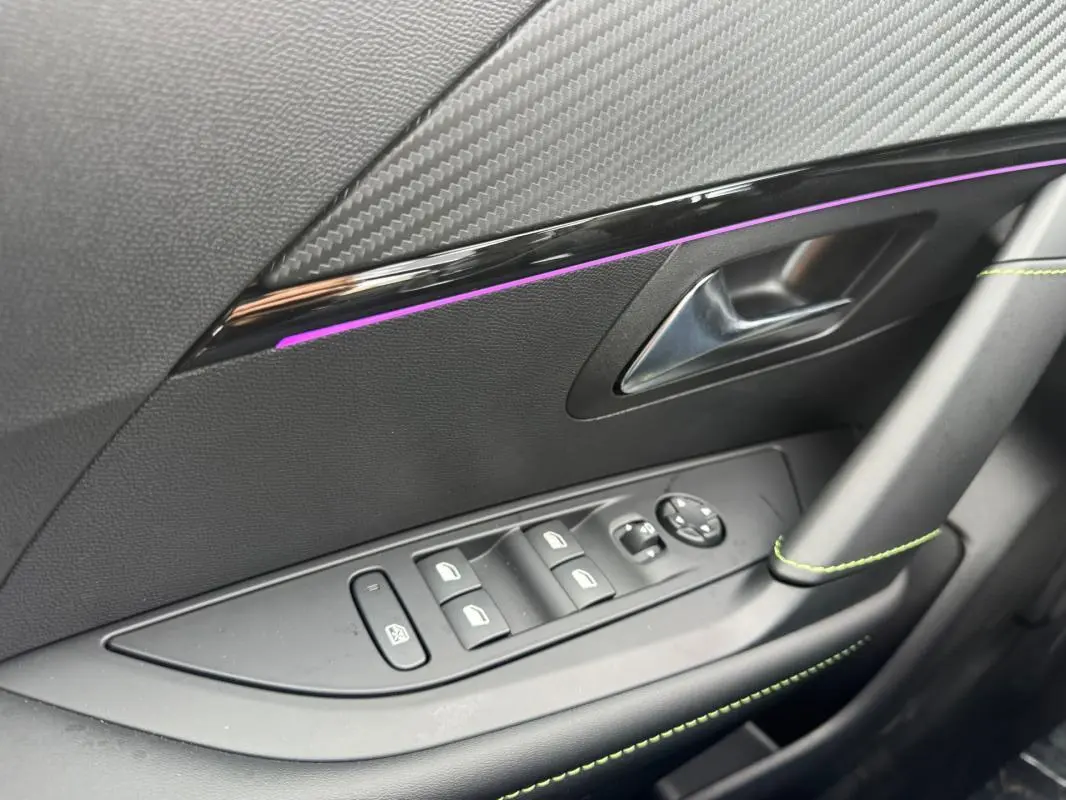 Détail de la porte côté gauche intérieure d'une Peugeot 208 Hybrid 110 gris, avec commandes vitres et insert décoratif noir brillant.