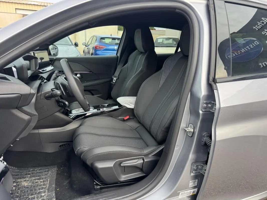 Intérieur avant droit d’une Peugeot 208 Hybrid 110 gris 2025, sièges noirs et tableau de bord moderne avec écran tactile.