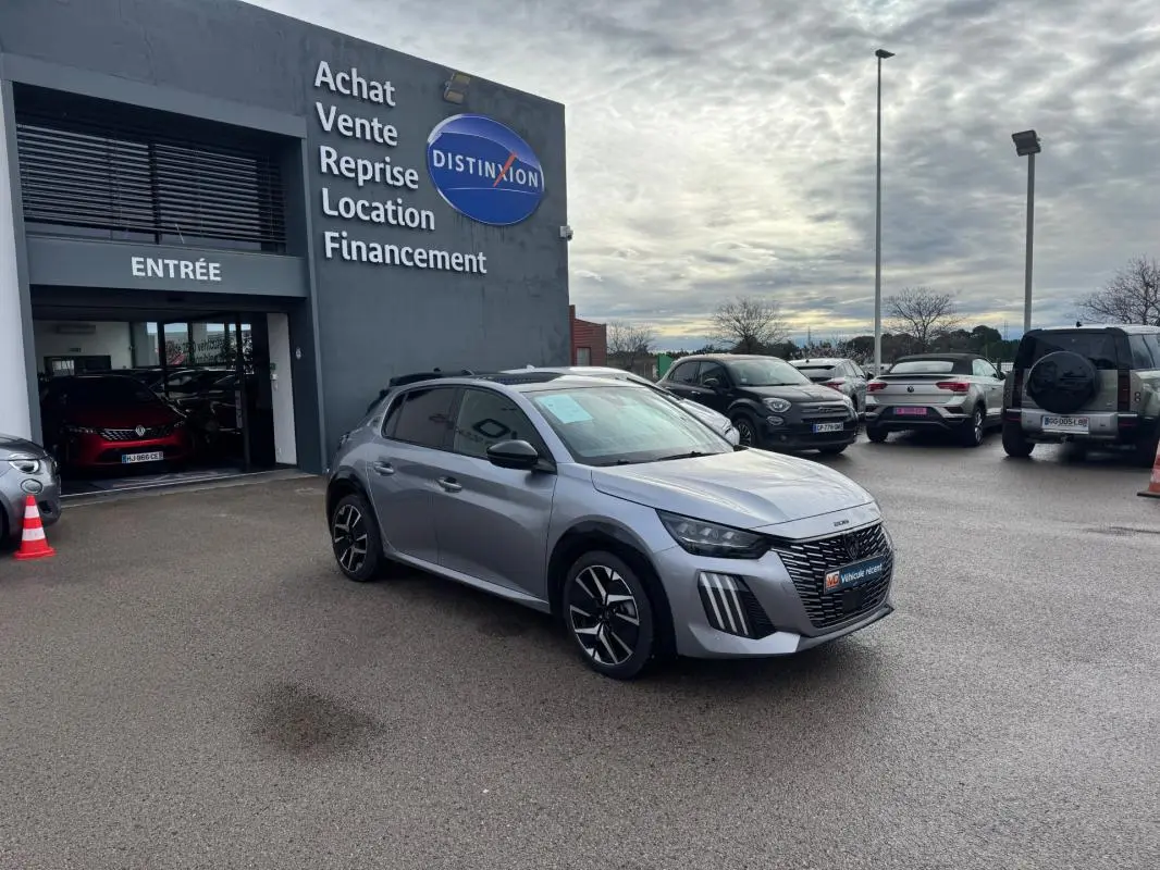 Peugeot 208 Hybrid gris vue 3/4 avant droit sur parking devant concession avec jantes alliage 17 pouces.