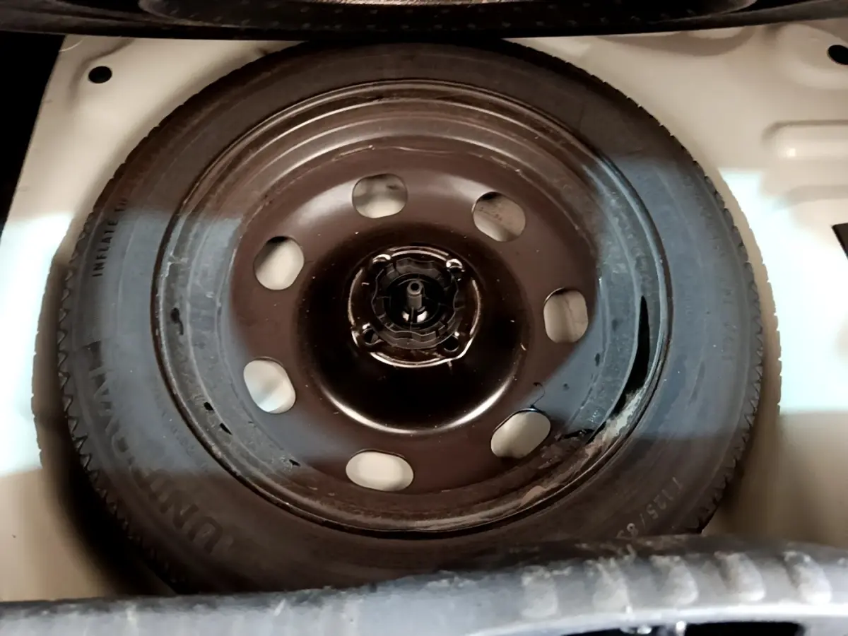 Roue de secours noire montée dans le coffre blanc d'une Citroën C3 BlueHDi 2022, vue de dessus.