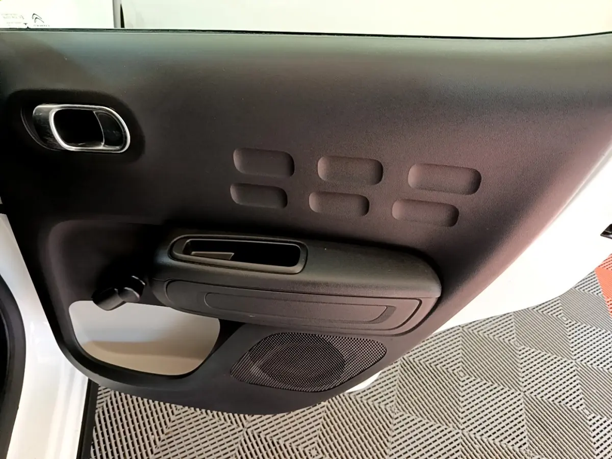 Vue rapprochée de la porte intérieure côté conducteur noire avec poignée et haut-parleur de la Citroën C3 blanche.